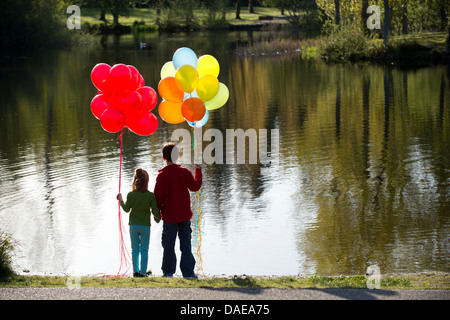 Brother and sister in front of lake with bunches of balloons Stock Photo