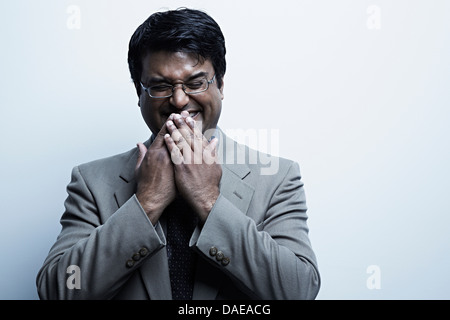 Studio portrait of mid adult male with hands over mouth laughing Stock Photo