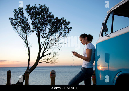 Young woman leaning on camper van at dusk Stock Photo