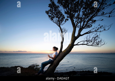 Young woman leaning on tree at dusk Stock Photo