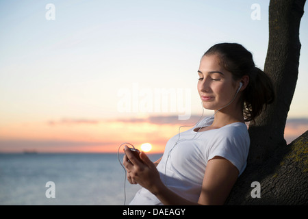 Close up of young woman leaning on tree at dusk Stock Photo