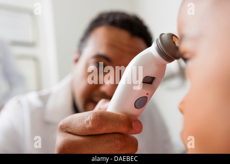 Mid adult doctor using medical equipment on young patient, close up Stock Photo