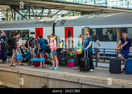 Tourists with suitcases and backpackers on vacation waiting on platform for train at railway station during the summer holidays Stock Photo