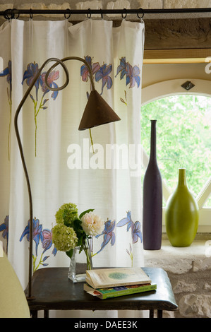Black lamp beside small table with vase of hydrangeas in front of window with blue iris patterned curtain Stock Photo