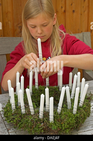 girl sticking candles on a wreath for the Advent season, Germany Stock Photo