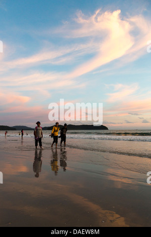 Thee Asian tourists walking on the Pantai Cenang beach in Langkawi during sunset, Malayisa Stock Photo