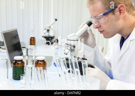A male medical or scientific researcher or doctor using a microscope in a laboratory with test tubes. Stock Photo