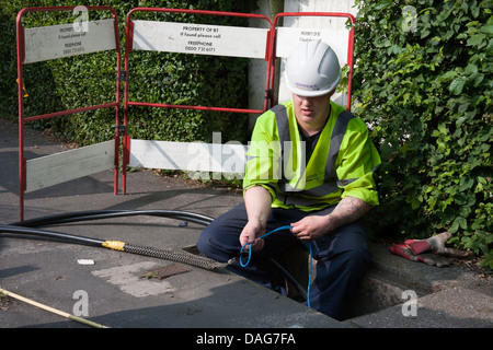 A BT Openreach telecommunications technician working in a manhole at the roadside, Southport, Merseyside, UK Stock Photo
