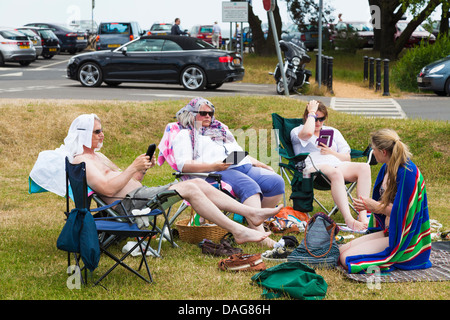 Family group sitting on grass by car park using e-readers. Stock Photo