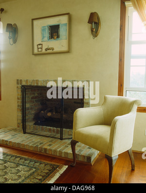White upholstered chair beside simple brick fireplace in coastal living room Stock Photo