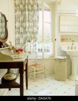 Marble topped washstand and white tiled floor in French country bathroom with blue floral curtains and pedestal washbasin Stock Photo