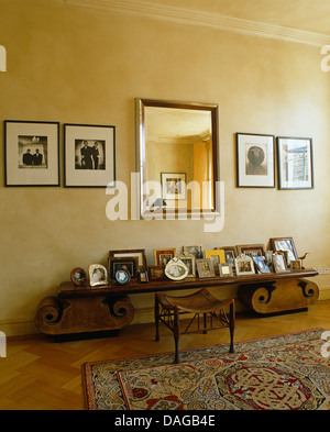 Framed black+white photographs on either side of mirror above low console table with framed family photographs in modern bedroom Stock Photo