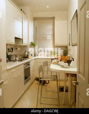 Modern white galley kitchen with chrome stools at breakfast bar set for breakfast. Stock Photo