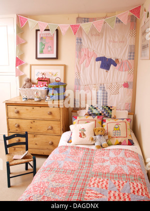 Quilt on wall above bed with hand made cushions and pink patchwork quilt in girl's bedroom with bunting and pine chest Stock Photo