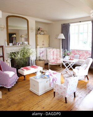 White wooden chest with pastel colored chairs and wooden flooring in cottage living room with large mirror above fireplace Stock Photo