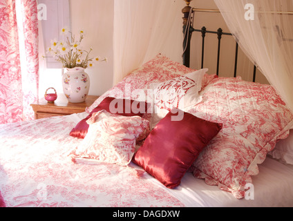 Pink silk cushions with pink Toile de Jouy quilted cushions and matching cover on brass bed with white voile drapes Stock Photo