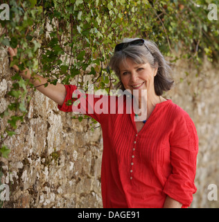 Portrait of smiling woman wearing a red top and standing beside stone wall Stock Photo