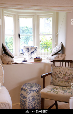 Hand worked tapestry cushion and seat on wooden chair beside Chinese blue+white porcelain stool below cottage window Stock Photo