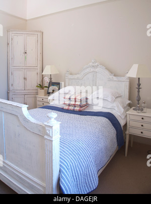 Blue striped quilt and white pillows on white painted bed bed in pale gray bedroom with white painted corner cupboard Stock Photo