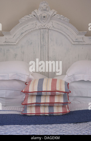 White pillows and striped cushions on double bed with painted  white wood headboard Stock Photo
