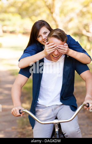 playful teen girl covering boyfriend's eyes with hands while riding a bike Stock Photo