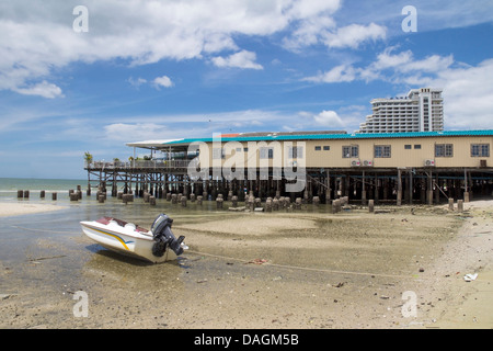 Boat with outboard motor on Town Beach, restaurant pier and Hilton hotel in the background, Hua Hin, Thailand Stock Photo