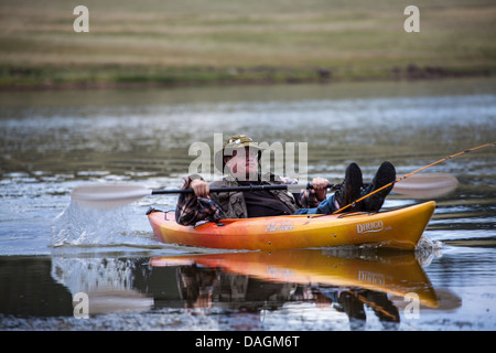 Young man paddling a yellow kayak in a lake in Arizona with his feet and fishing pole propped up on the front of the kayak. Stock Photo