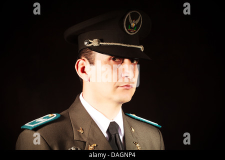 A close-up portrait of a male military officer wearing a formal uniform, including a dark service cap with an embroidered emblem and a braided band, a brown jacket with teal shoulder boards, and a Stock Photo