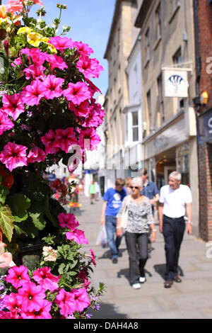 Wells Somerset colourful hanging basket flowers along the High Street with shoppers and visitors Stock Photo