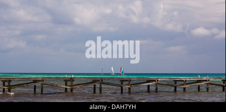 Sailboats on the turquoise Caribbean sea behind a wooden landing in the foreground. Stock Photo