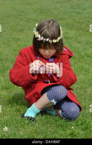 Six year old girl making a daisy chain on the grass. Model Released Stock Photo