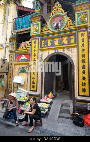 Vietnamese street vendors selling fruit outside a Chinese temple in the Old Quarter, Hanoi, Vietnam Stock Photo