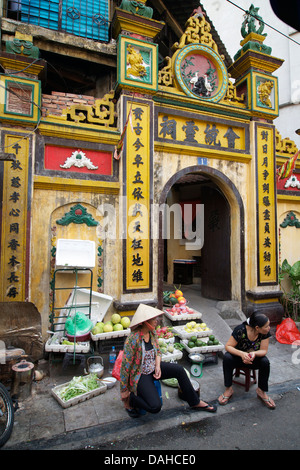 Vietnamese street vendors selling fruit outside a Chinese temple in the Old Quarter, Hanoi, Vietnam Stock Photo