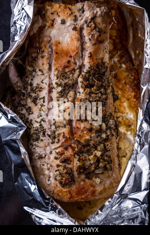 baked pork meat with seasoning in foil on black tray Stock Photo