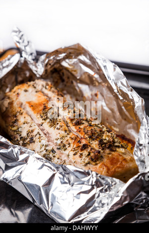 baked pork meat with seasoning in foil on black tray Stock Photo