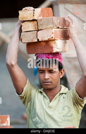 A laborer carries bricks on his head at a construction site in the historic old city of Dhaka Bangladesh Stock Photo