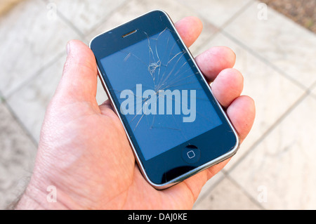 Mans hand holding an Apple iPhone with cracked screen Stock Photo