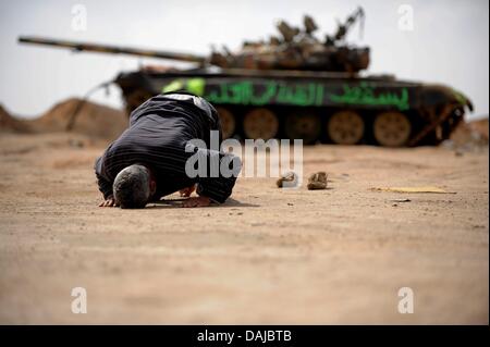 The Libyan insurgent Muftah El Shahomi prays in front of a destroyed tank in Ajdabiya, Libya. Muammar Al-Gaddafi has rejected a rebel proposed ceasefire. Photo: MAURIZIO GAMBARINI Stock Photo