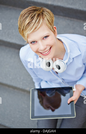 Woman with tablet computer and headphones sitting on stairs Stock Photo