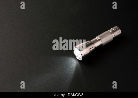 Flashlight lying on a dark gray background. Light is on. Stock Photo
