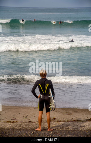 Wearing a wet suit for the cold water, a teenage boy member of the San Clemente, CA, High School surfing team prepares to surf. Stock Photo