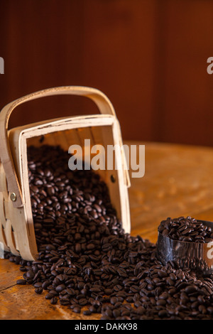 Coffee beans spilling from a birchwood basket on an antique oak table Stock Photo
