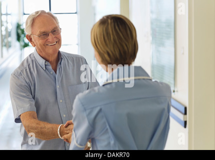 Older patient and nurse shaking hands in hospital Stock Photo