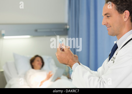 Doctor checking syringe in hospital room Stock Photo