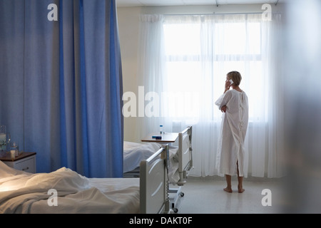 Patient in gown talking on cell phone in hospital room Stock Photo