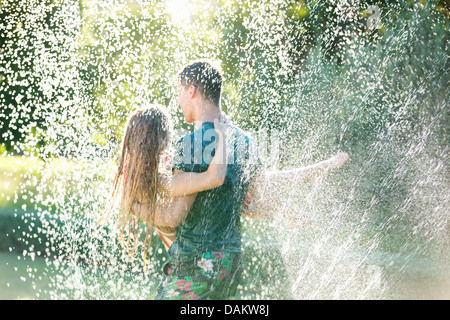 Couple playing in sprinkler in backyard Stock Photo