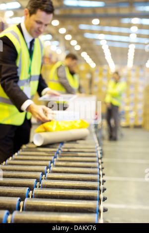 Businessman checking packages on conveyor belt in warehouse Stock Photo