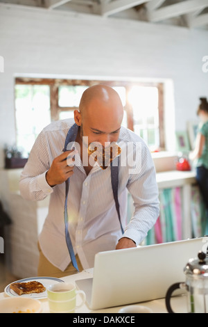Businessman eating breakfast and using laptop Stock Photo