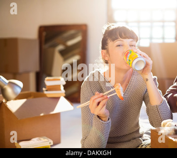 Woman drinking soda and eating sushi in new home Stock Photo