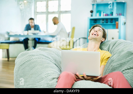 Laughing man using laptop in beanbag chair Stock Photo